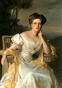 Portrait assis d'une jeune femme portant une robe claire avec un large décolleté.