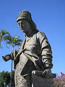 Photographie en couleurs. La statue d'Amos représentée en buste : il est souriant, une main levée et l'autre portant un grand parchemin.
