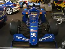 Photographie d'une monoplace de Formule 1 bleu foncé, exposée dans un musée automobile, près d'autres voitures.