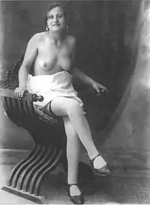 Image d'une jeune femme borgne à la poitrine dévêtue, assise jambes croisées.