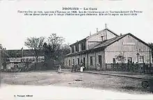 Carte postale de 1918. Quelques personnes devant le bâtiment de la gare à droite. Au centre une esplanade en terre battue.