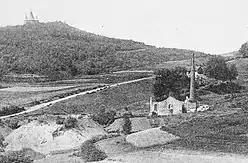 Photo noir et blanc montrant une ruine et une cheminée d'usine au pied de la colline de la chapelle Notre-Dame-du-Haut.