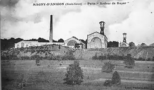 Photo noir et blanc un ensemble de bâtiments industriels typés 1900 avec deux grand chevalements (tour avec bigue) métalliques et cheminée d'usine.