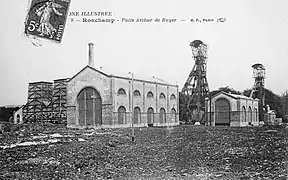 Photo noir et blanc montrant deux grands bâtiment typés 1900 avec de grandes baies vitrés arrondies, à l'arrière les deux chevalements.