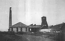 Photo noir et blanc de petits bâtiments, avec cheminée et tour pyramidale en bois fermée.