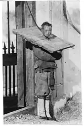 Photographie en noir et blanc montrant un homme se tenant debout, prisonnier d'une cangue.