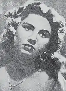 Image en noir et blanc, plein cadre d'un visage féminin, cheveux noirs bouclé, avec boucle d'oreille et collier.