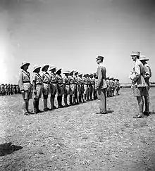 Photo du général de Gaulle s'adressant à une rangée d'une vingtaine de militaires au garde-à-vous devant le front des troupes