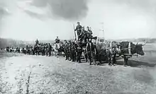 Photo en noir et blanc d'un convoi de chariots tirés par des bœufs avec des hommes en uniforme et en civil dans une plaine