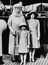 Une femme âgée en compagnie de deux filles portant des pardessus et des chapeaux. Le groupe semble se trouver sur la passerelle d'un navire.