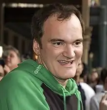 Photo de Quentin Tarantino s'arrêtant à la poitrine. Il sourit et porte une veste de jogging.