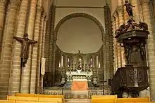 Photographie d'un chœur d'église avec un crucifix vêtu suspendu au pilier gauche et une chaire à prêcher sur le pilier droit
