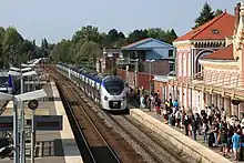 Train régional bimode composé de deux éléments de six caisses chacun, s'approchant des quais de la gare par temps ensoleillé et devant une affluence voyageurs importante.