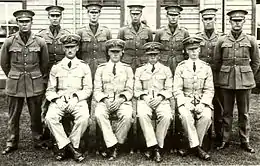 Portrait en noir et blanc de onze hommes en tenue militaire et coiffés de casquettes à visière, sept d'entre eux sont debout et quatre assis