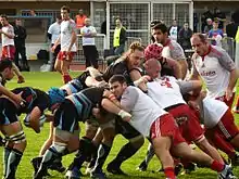 Pendant un match de rugby, un joueur progresse avec un ballon derrière un maul disputé.