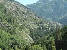 route étroite à flanc de montagne, dans une forêt peu dense.