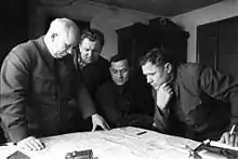 Photographie de plusieurs hommes en uniforme examinant une carte posée sur une table