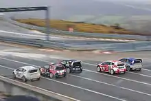 Photographie de cinq voitures de rallycross, vue de derrière, s'élançant, alignées, de différentes couleurs.