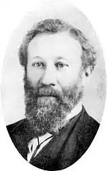 Portrait d'un homme avec une longue barbe bouclée, avec des cheveux partant sur le côté gauche.