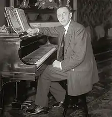 Black and white photograph of a thin, clean-shaven man seated at a piano