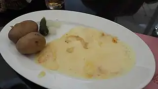 Raclette servie avec des pommes de terres et des petits oignons.