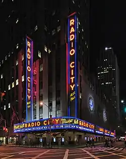 Immeuble new-yorkais illuminé avec plusieurs fois le nom Radio City Music Hall, à la verticale et l'horizontale.