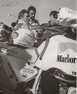 Photographie de trois hommes discutant derrière une moto sportive.