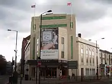 Un bâtiment rectangulaire beige avec deux traits verts horizontaux à son sommet.