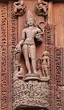 Statue en pierre représentant une divinité hindoue souriante, debout sur un socle