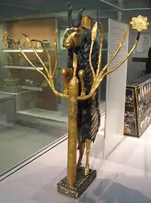 Figurine noire et or d'un bouquetin dressé sur ses pattes arrières pour accéder à un arbre.