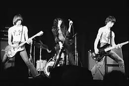 photo en noir et blanc de trois hommes en jean et blouson en cuir noirs sur scène.