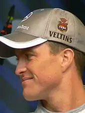 R.Schumacher, de profil, porte une casquette grise et sourit.