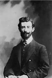 Photo noir et blanc en buste d’un homme barbu et moustachu portant veste et cravate.
