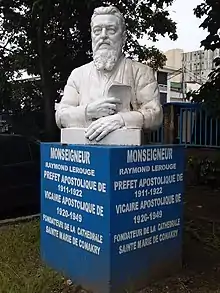 Photographie couleur du buste en pierre d'un homme barbu, sur un socle bleu.