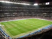 Vue intérieure du stade madrilène de football un soir de match. Le terrain est éclairé et les tribunes remplies de spectateurs.