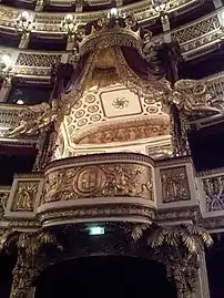 Un balcon richement décoré ; toit avec draperies et chapeau en forme de couronne royale.