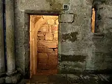 Photographie d'une partie sombre de l'église : on distingue un passage dans l'épaisseur du mur et une fente