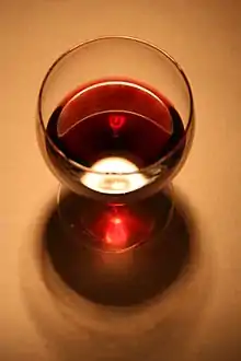 L'illustration en couleur montre un verre de vin pris par dessus. Le vin limpide et brillant est de couleur rouge rubis nuancé de brun. Le reflet sur la table donne une couleur rose très brillante