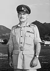 Demi-portrait en extérieur d'un homme moustachu en uniforme militaire d'été avec une casquette à visière.