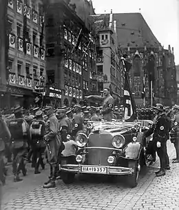 Photographie en noir et blanc de Hitler pendant le congrès du parti de 1935 à Nuremberg. Debout dans une voiture décapotable, il fait le salut nazi à ses partisans qui défilent