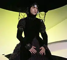 Femme maquillée qui porte une robe noire et un foulard.