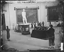 Photographie d'un cercueil entouré de soldats en armes au pied d'une statue blanche de Lincoln.