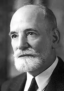 Photographie en noir et blanc, de trois quarts, du visage d’un homme portant une moustache et une barbe courte.