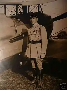 Photographie noir et blanc d'un homme se tenant debout, en uniforme, contre un biplan.