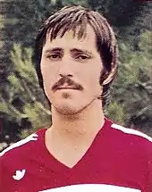 Photographie colorisée du haut d'un homme vu de face en tenue rouge de footballeur.
