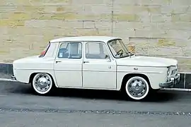 Une petite voiture blanche garée devant un mur de pierre.
