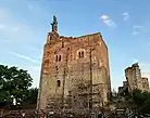 Photographie en couleurs d'un donjon surmonté d'une statue.