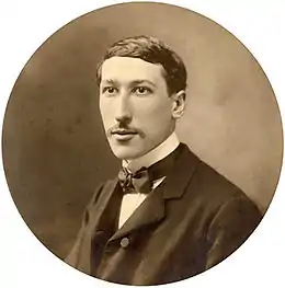 Photographie présentant en médaillon René Guénon au niveau du buste et tourné de trois quarts, moustachu, portant un habit noir sur une chemise blanche avec nœud-papillon