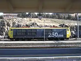 La photo couleur montre une locomotive à six essieux de couleur bleu foncé à faces jaunes à quai en gare d'Ávila.