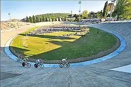 Photographie d'un vélodrome en plein air avec quatre coureurs en piste.